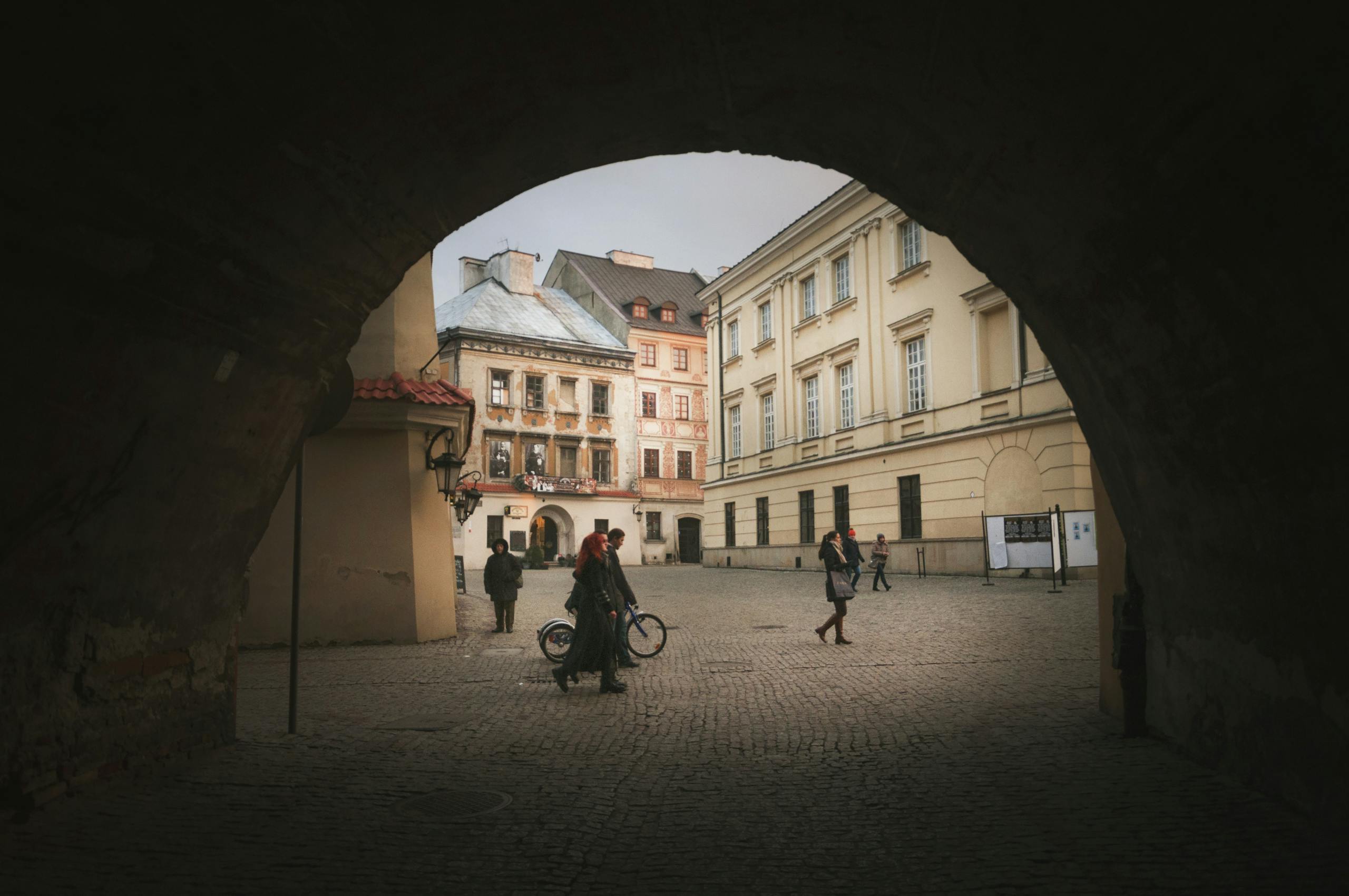 A historic street in Lublin, Poland, framed by a stone archway capturing daily life.