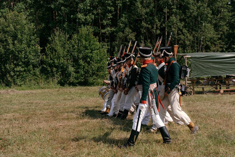 Group of soldiers in historical uniforms marching during a reenactment event outdoors.