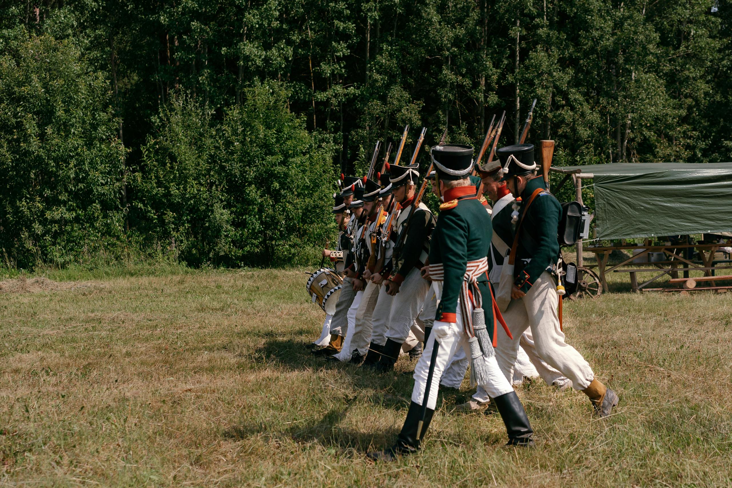 Group of soldiers in historical uniforms marching during a reenactment event outdoors.