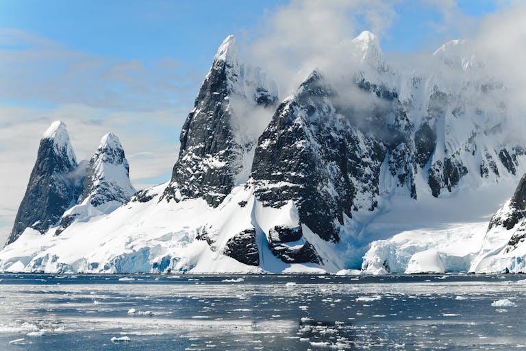 Majestic snowy peaks rise over icy Antarctic waters, showcasing untouched nature.
