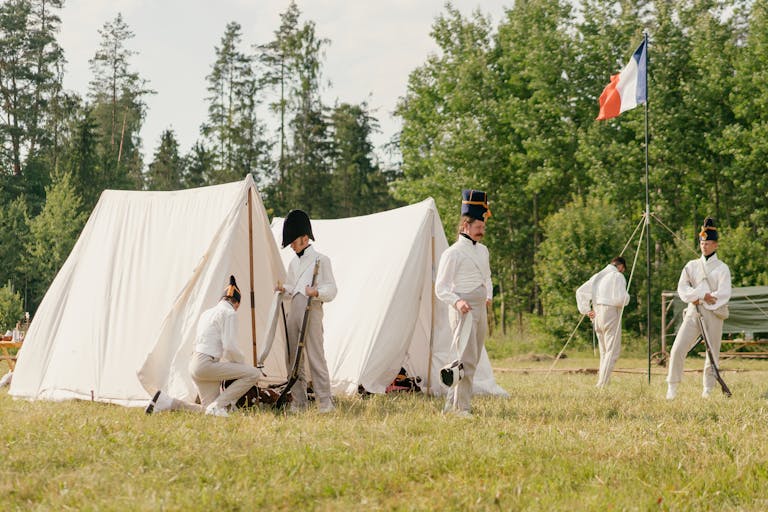 Men in Napoleonic uniforms reenacting a military camp scene outdoors.