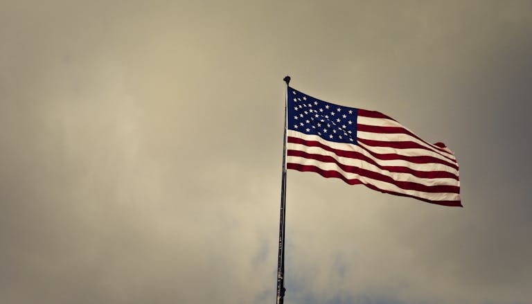 US flag waving in wind against a cloudy sky, symbolizing freedom and patriotism.